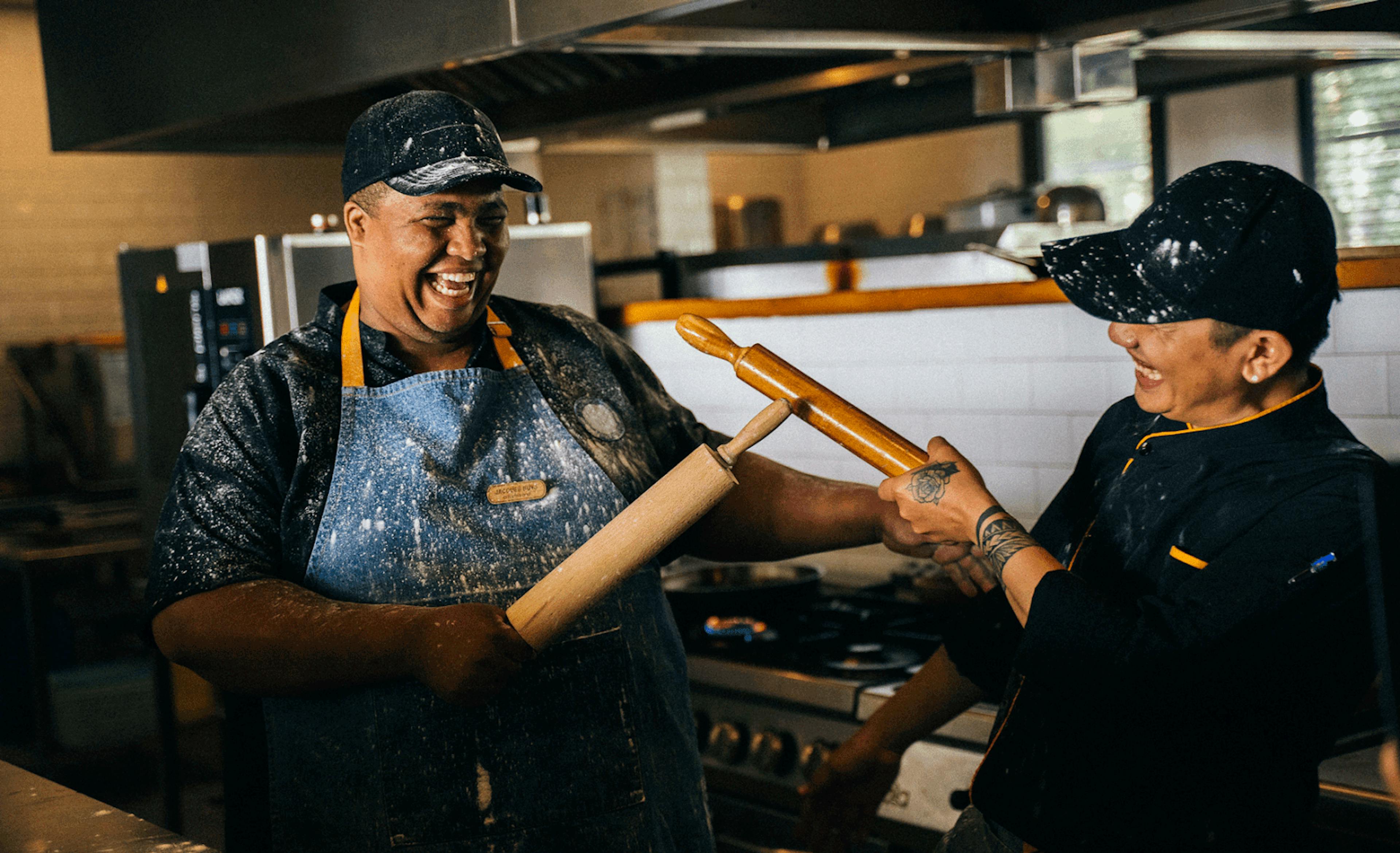 Image of two restaurant employees smiling while holding rolling pins