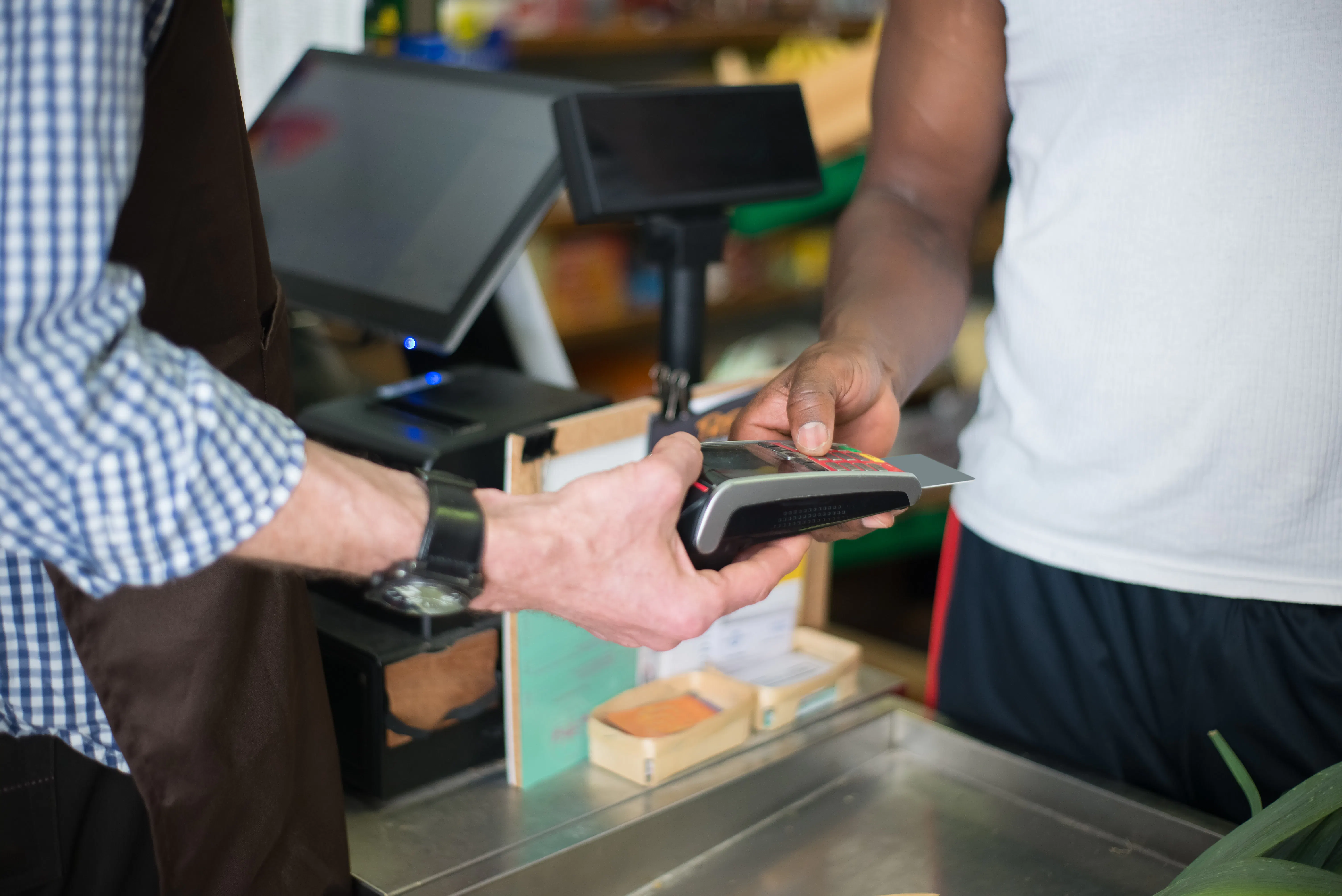 Cashier handing POS to customer at grocery store.