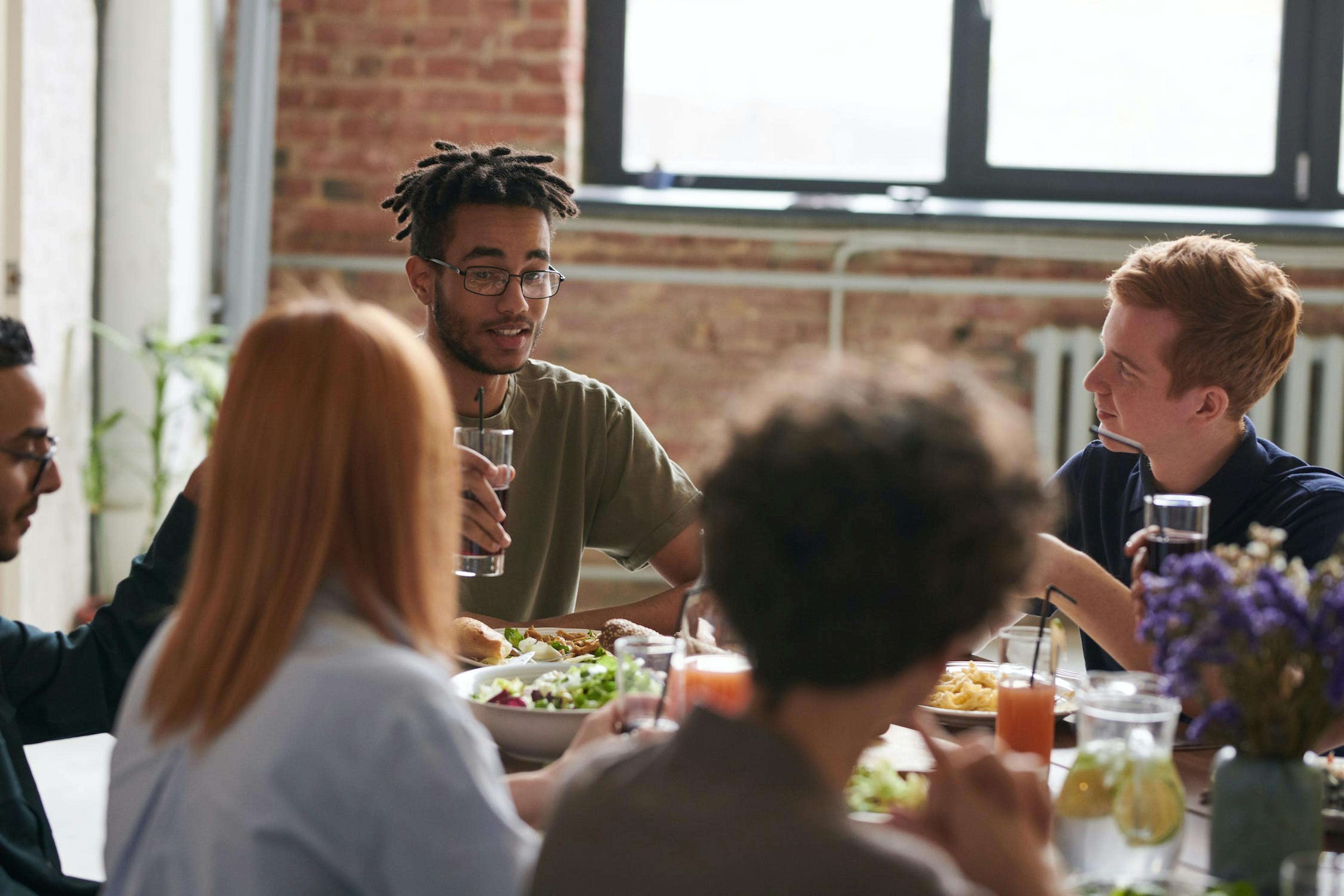 Group of Gen Z friends eating around a table. 