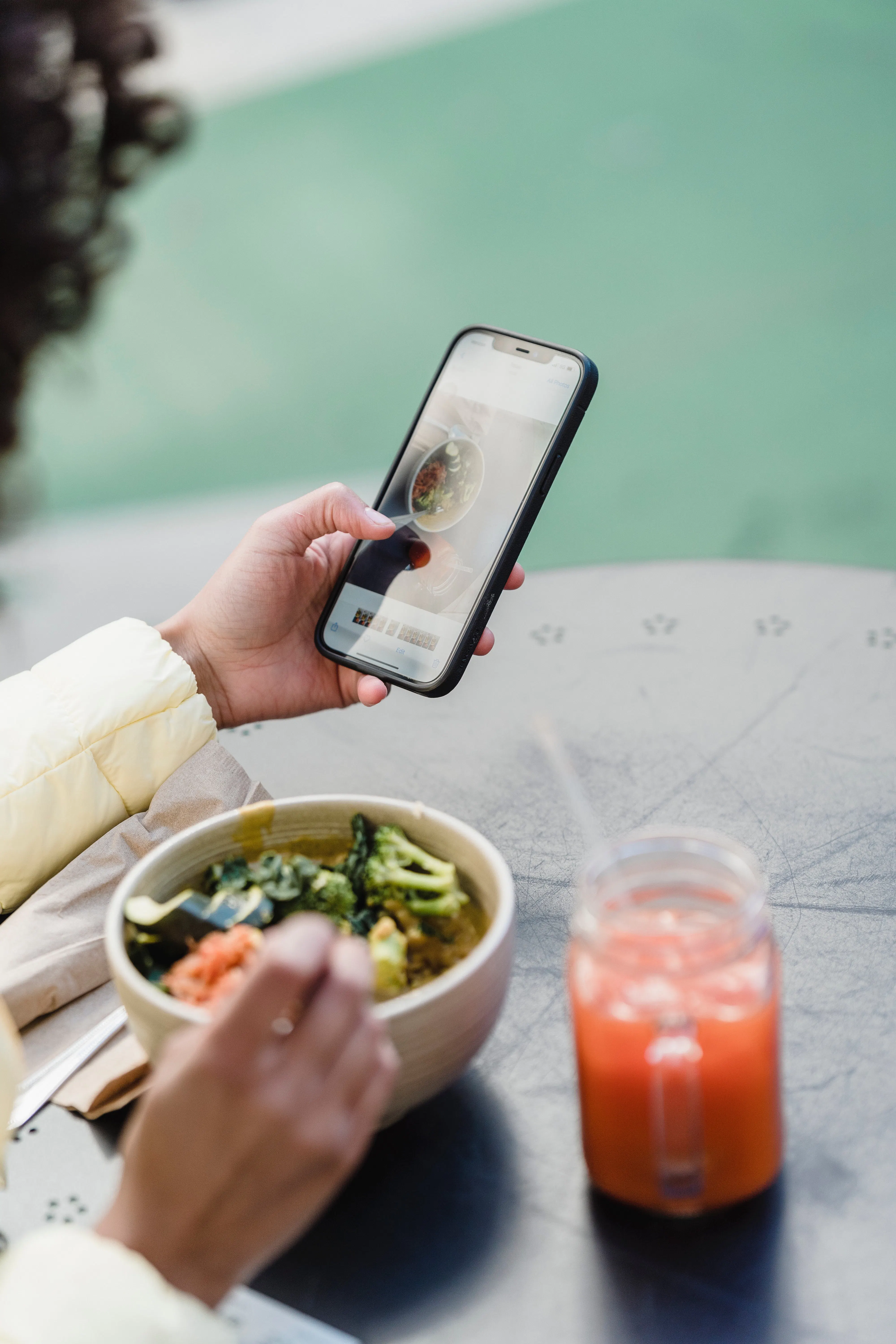 Woman using iPhone while eating a salad and enjoying a pink beverage. 
