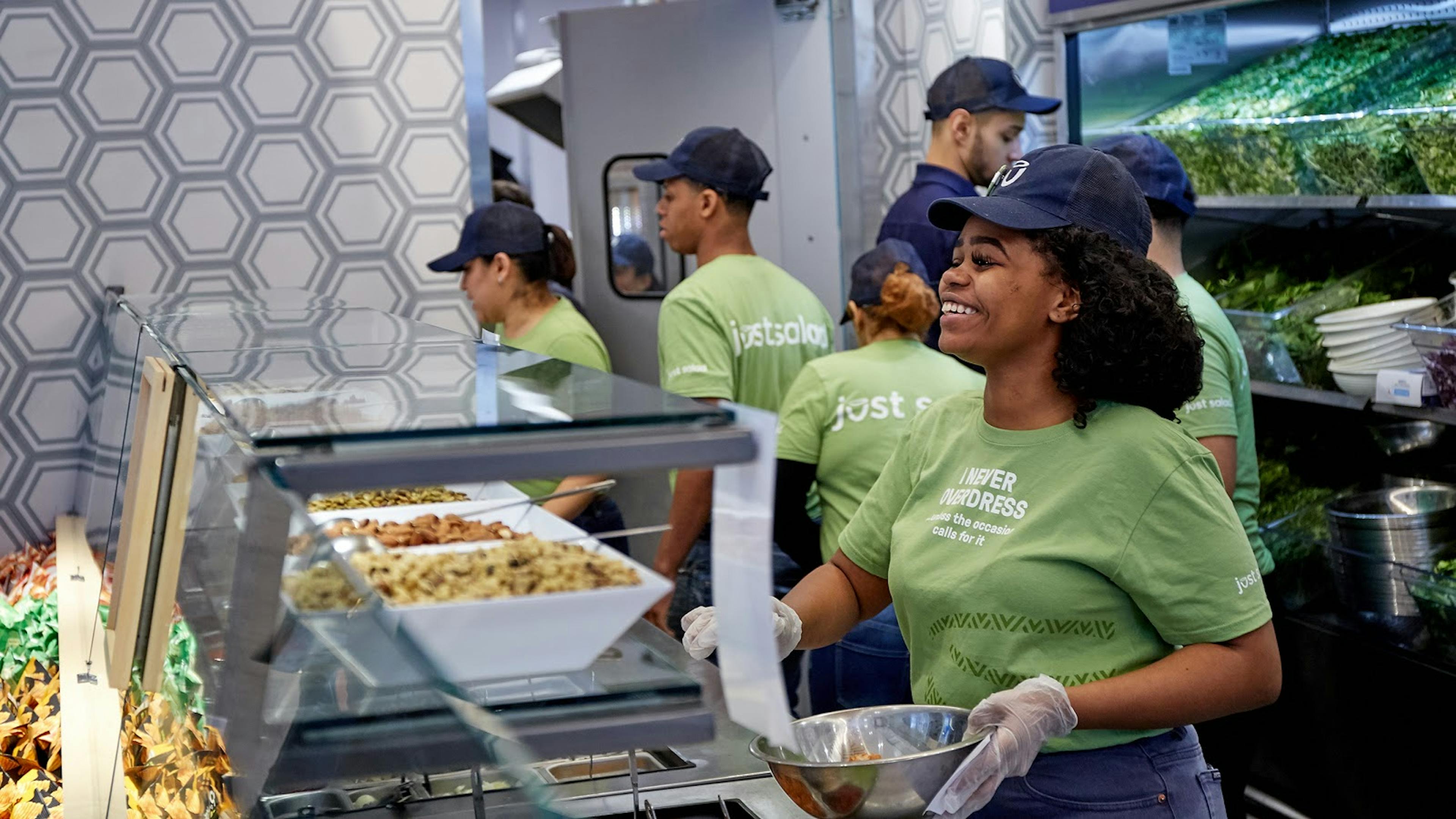 Image of smiling Just Salad employee preparing a salad for a guest