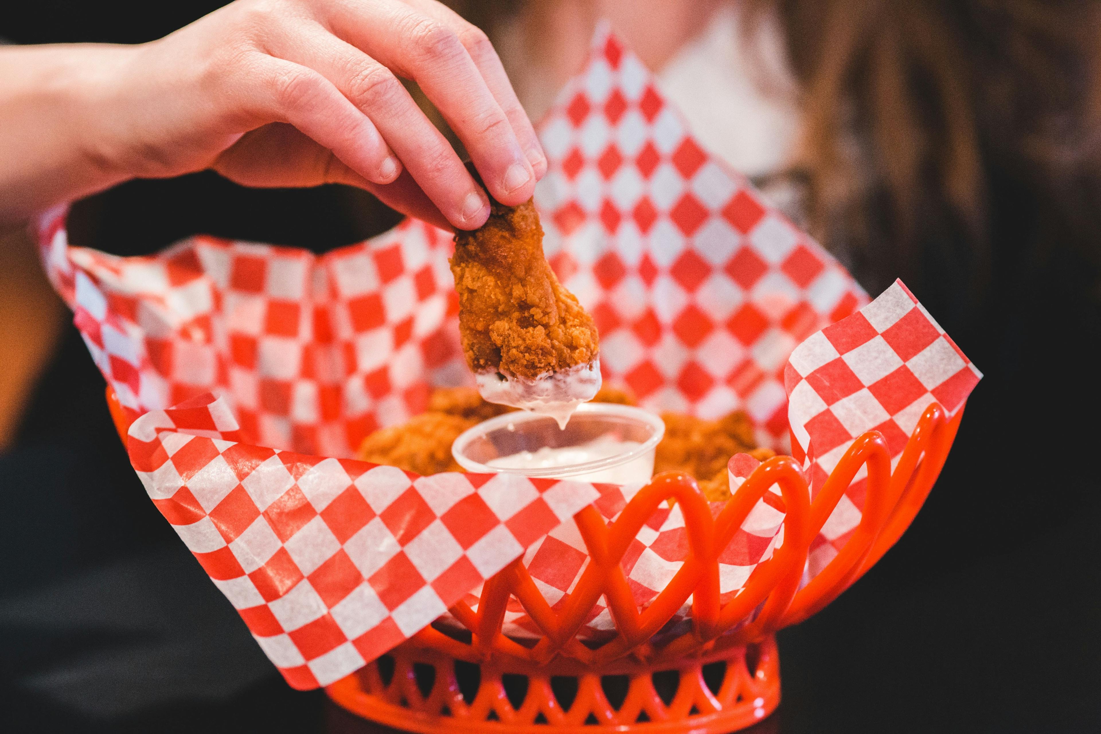 Woman's hands dipping chicken finger in sauce at a restaurant.