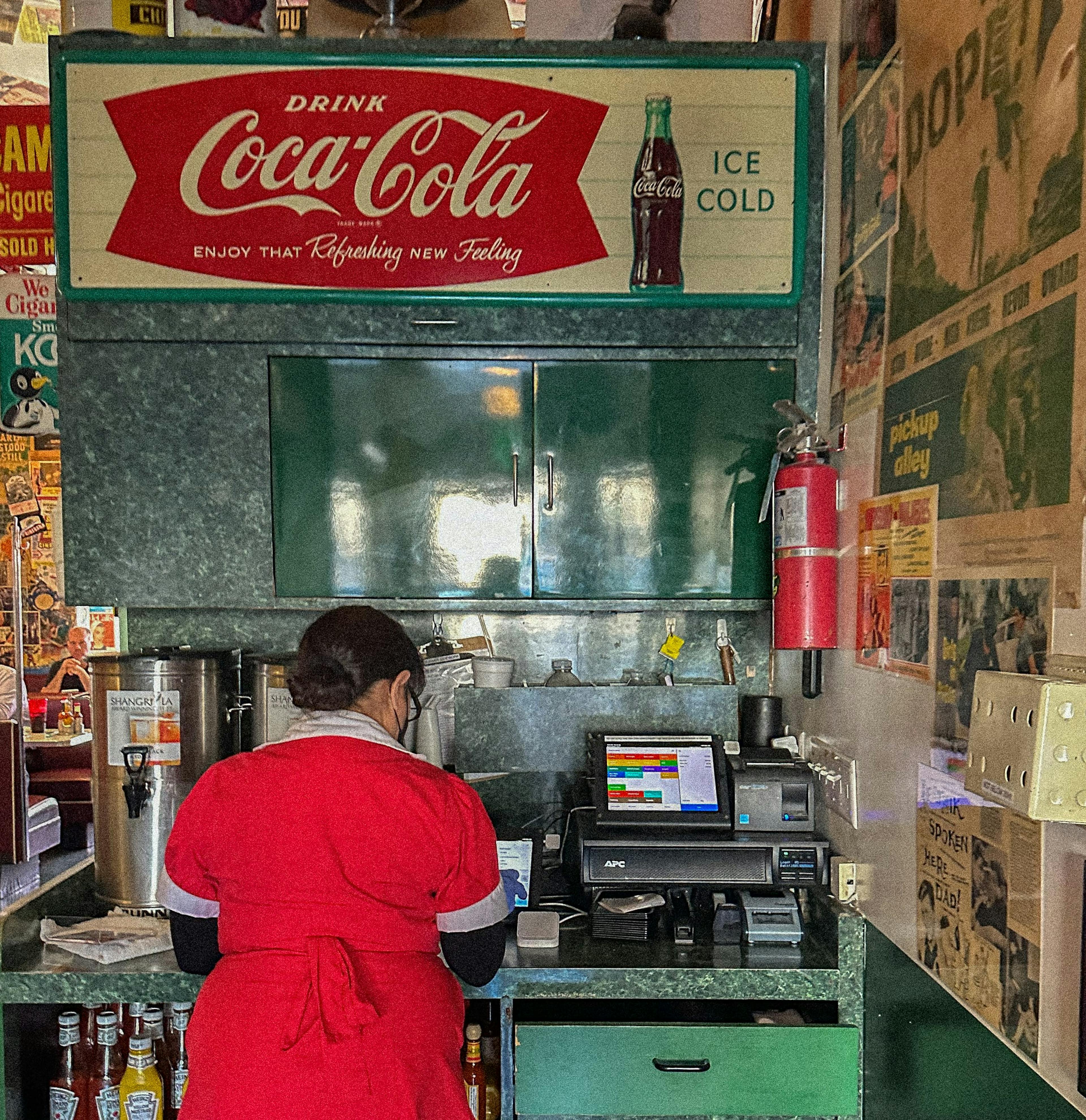 Restaurant worker at cash register under an old-fashioned Coca-Cola sign. 