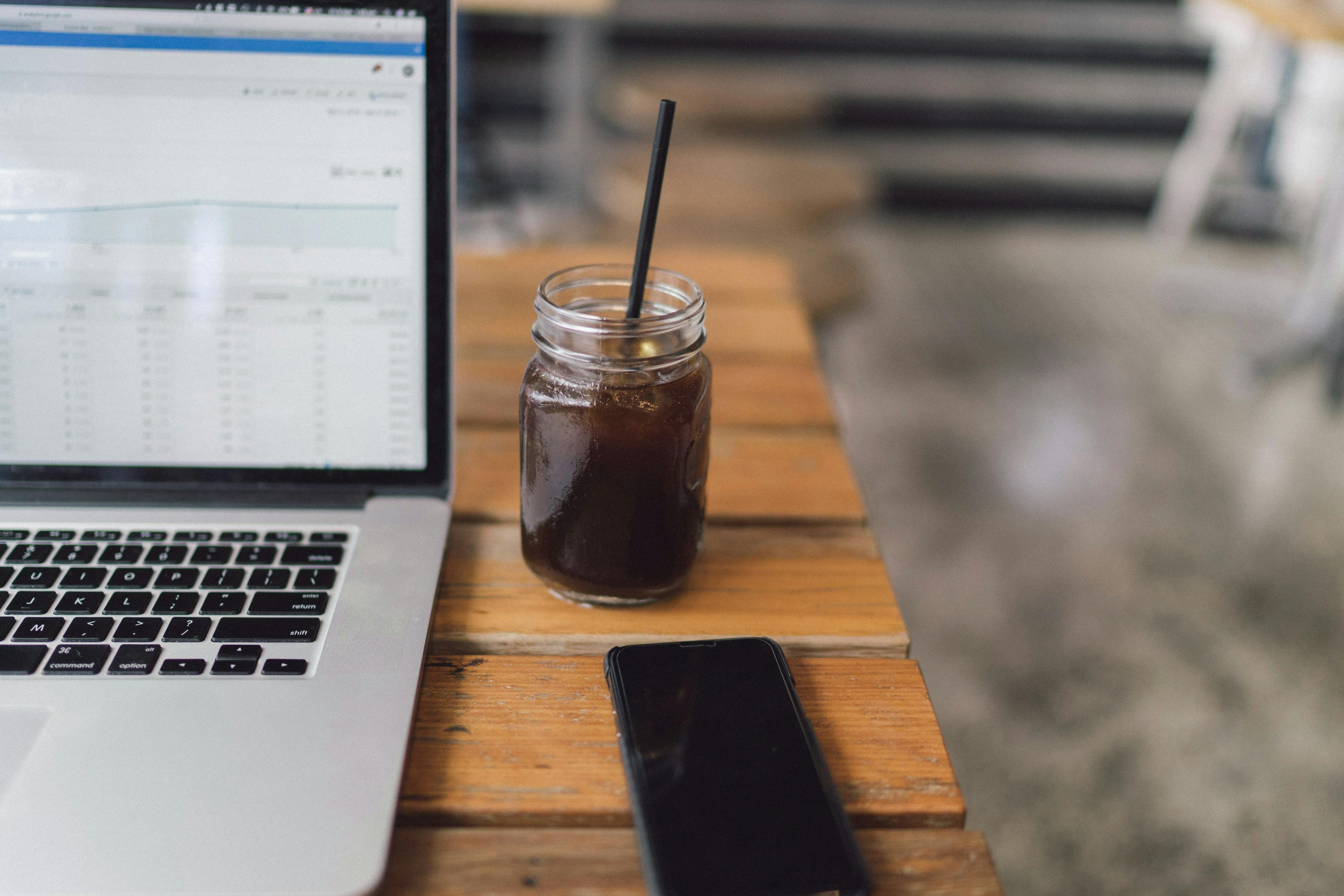 Open computer spreadsheet with coffee and iPhone on table.