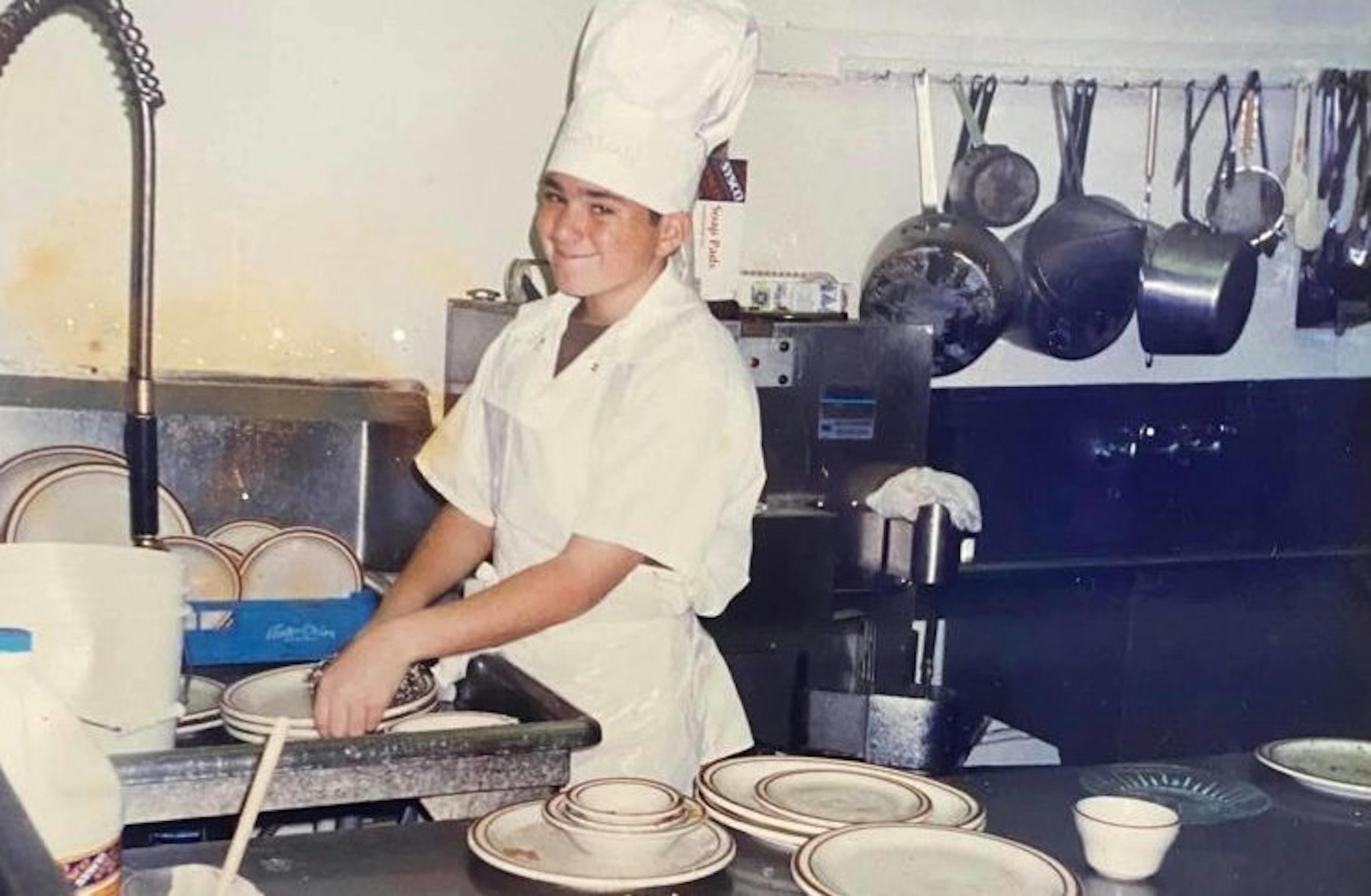 Image of a young Shawn Walchef wearing a chefs hat, cooking in the kitchen of his family restaurant