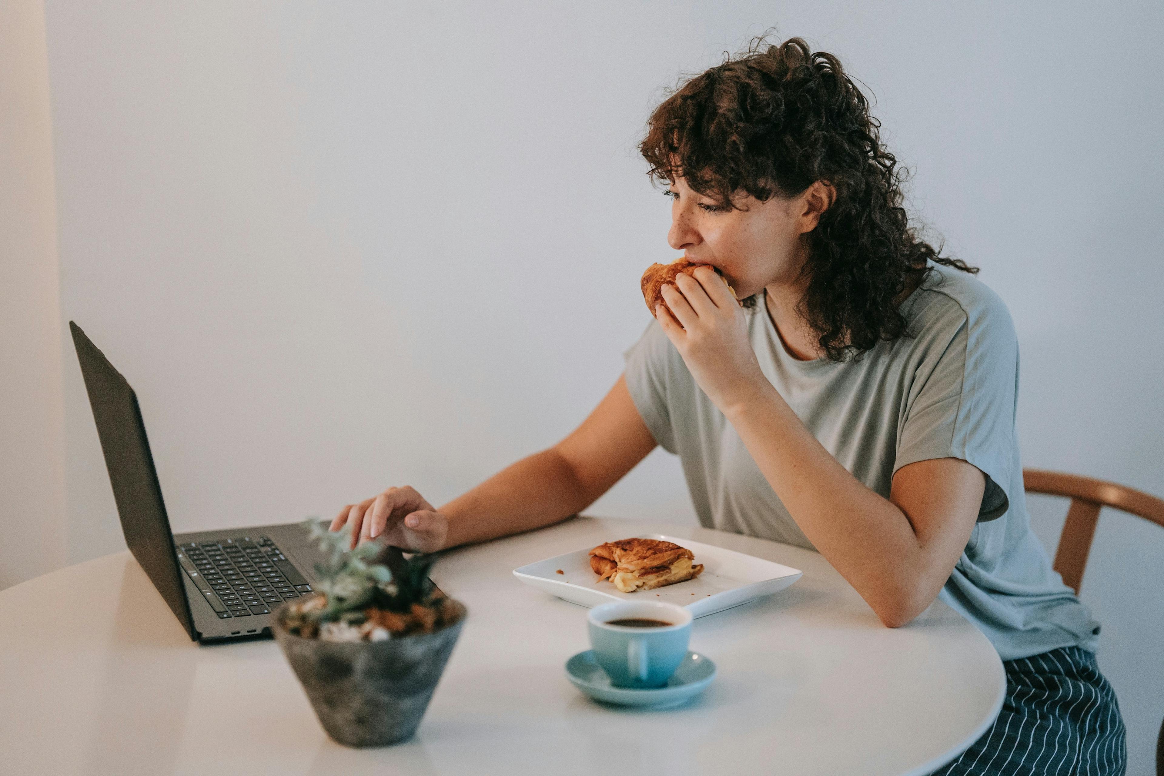 Image of someone eating a food delivery meal at home while looking at their laptop