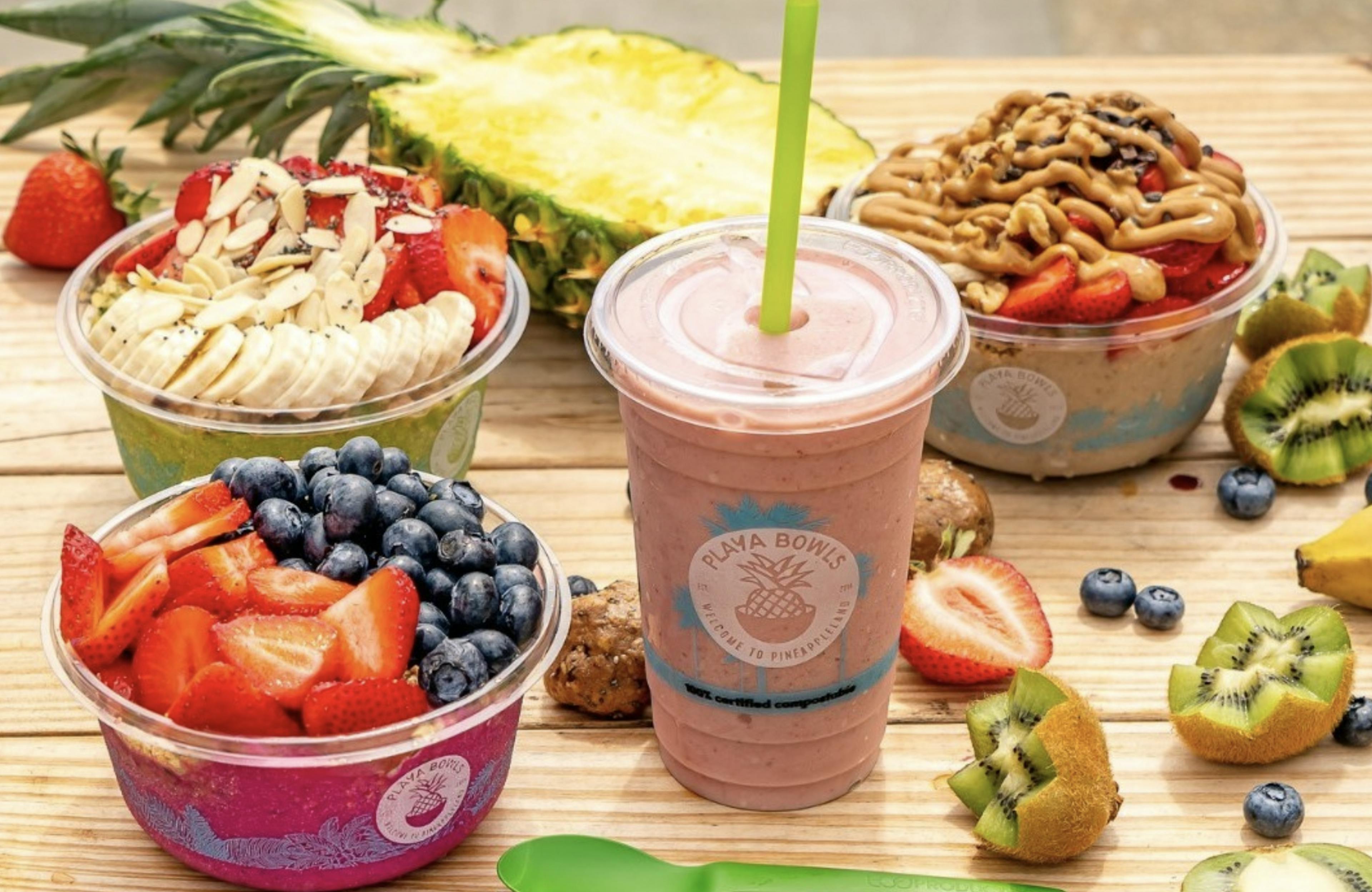 Image of 3 Playa Bowls acai bowls and one smoothie on a table with assorted fruits in the background