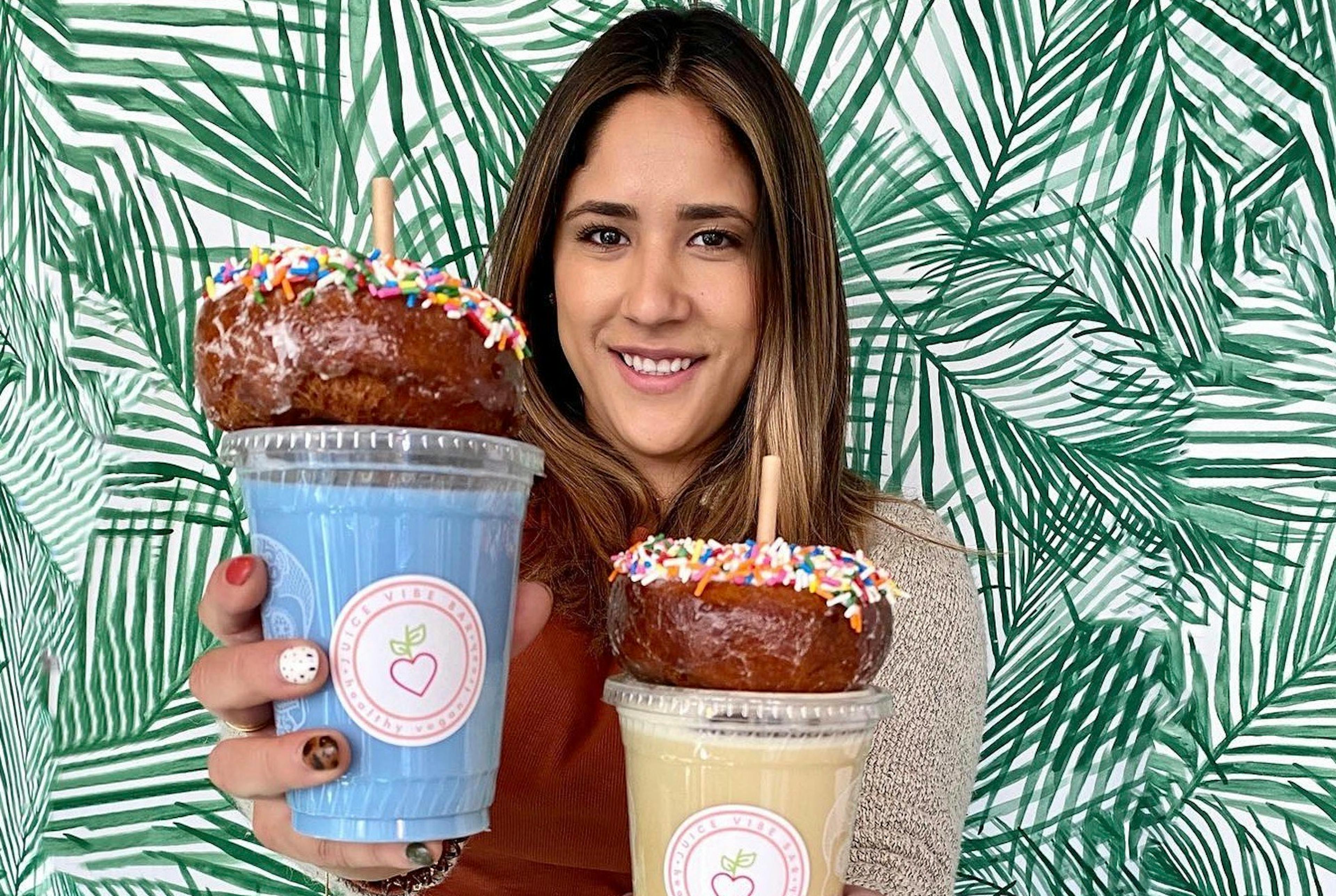 Image of Anabelle Martinez, owner of Juice Vibe Bar, holding two smoothies with donuts on top of each cup