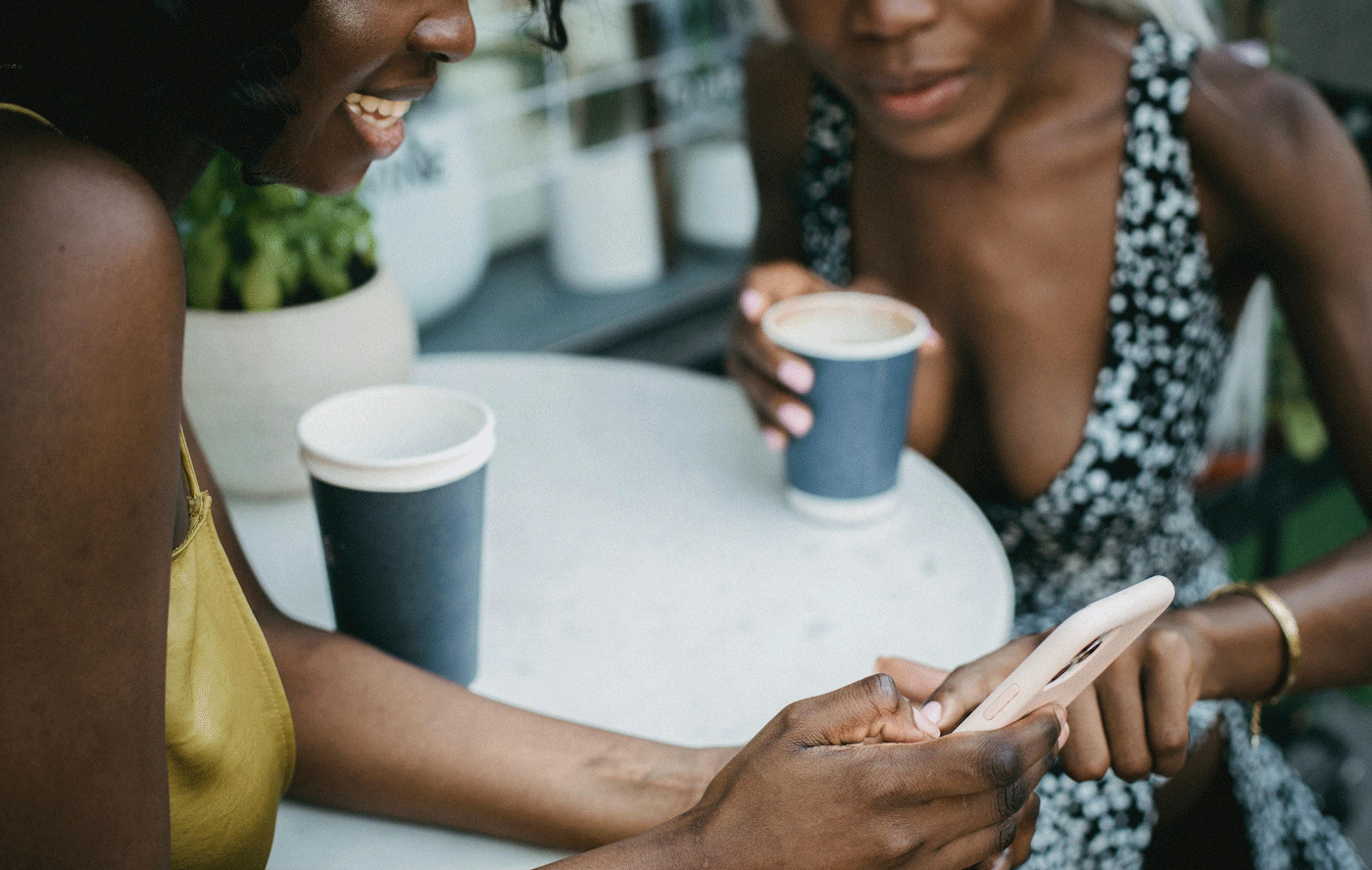 Image of two women looking at an iPhone while enjoying a cup of coffee at a café