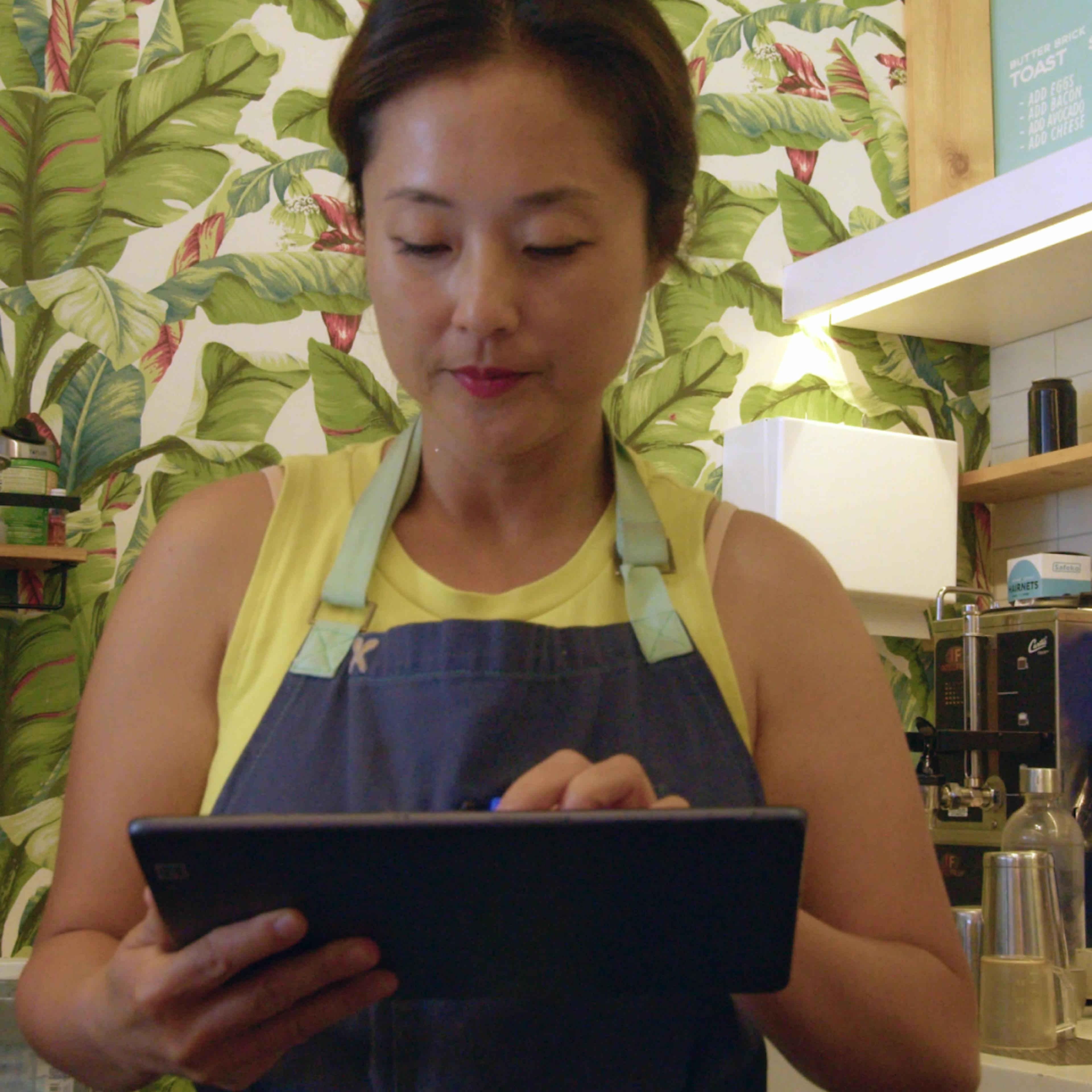 Image of a woman restaurant owner managing orders from a single delivery tablet