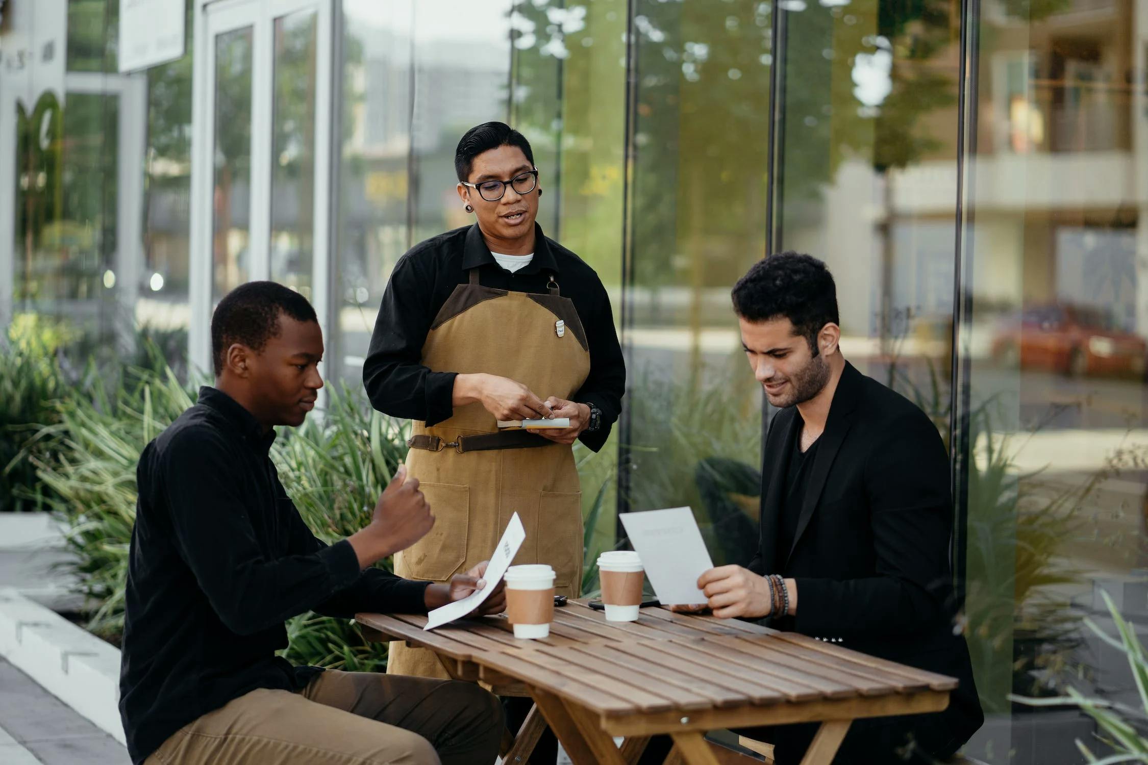 Customers holding menu and ordering from server on outdoor patio.