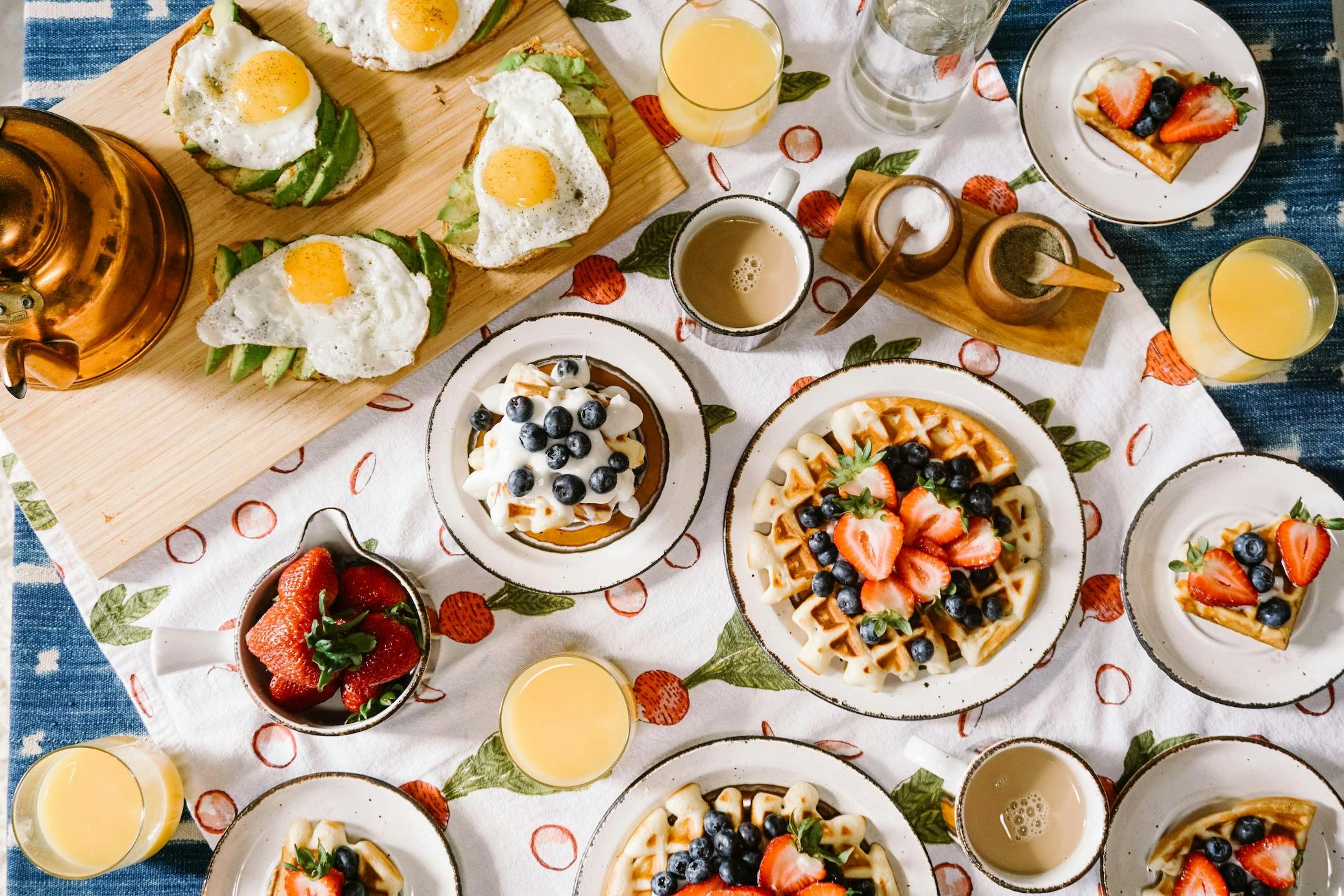 Restaurant table with waffles, eggs, fresh fruit and orange juice.