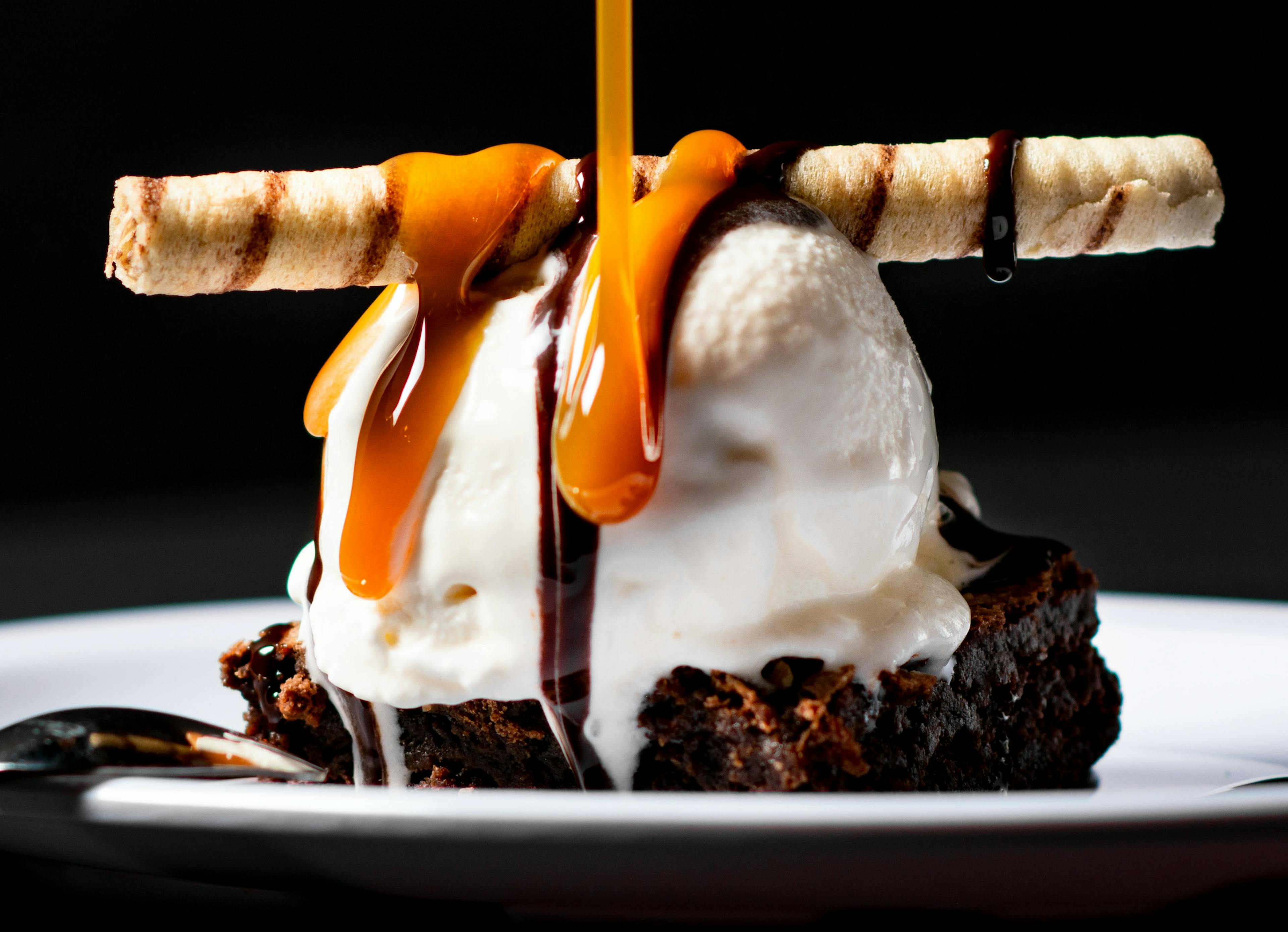 A scoop of ice cream, drizzled with caramel, on a brownie. 