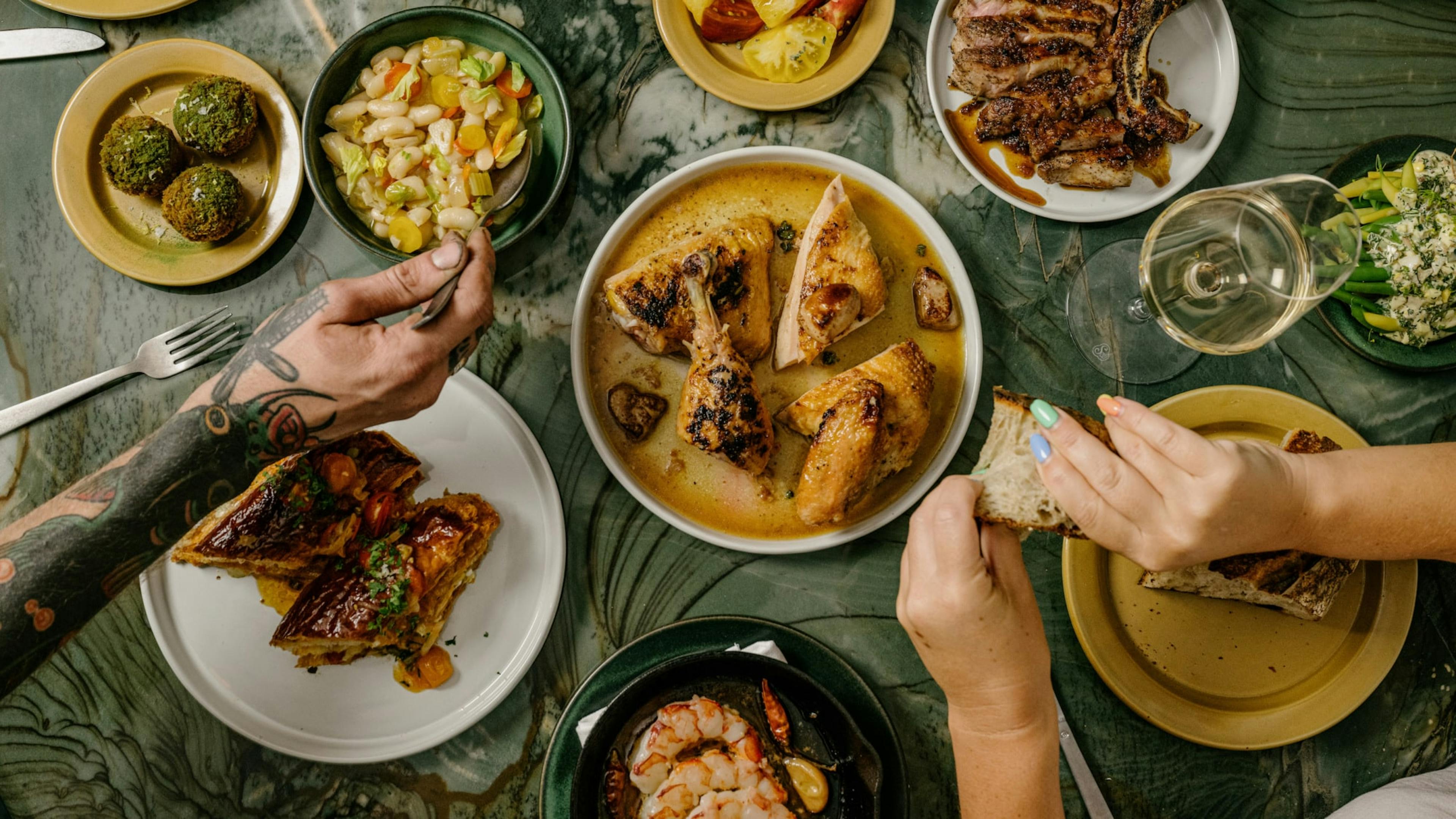 People reaching over plates of food. 