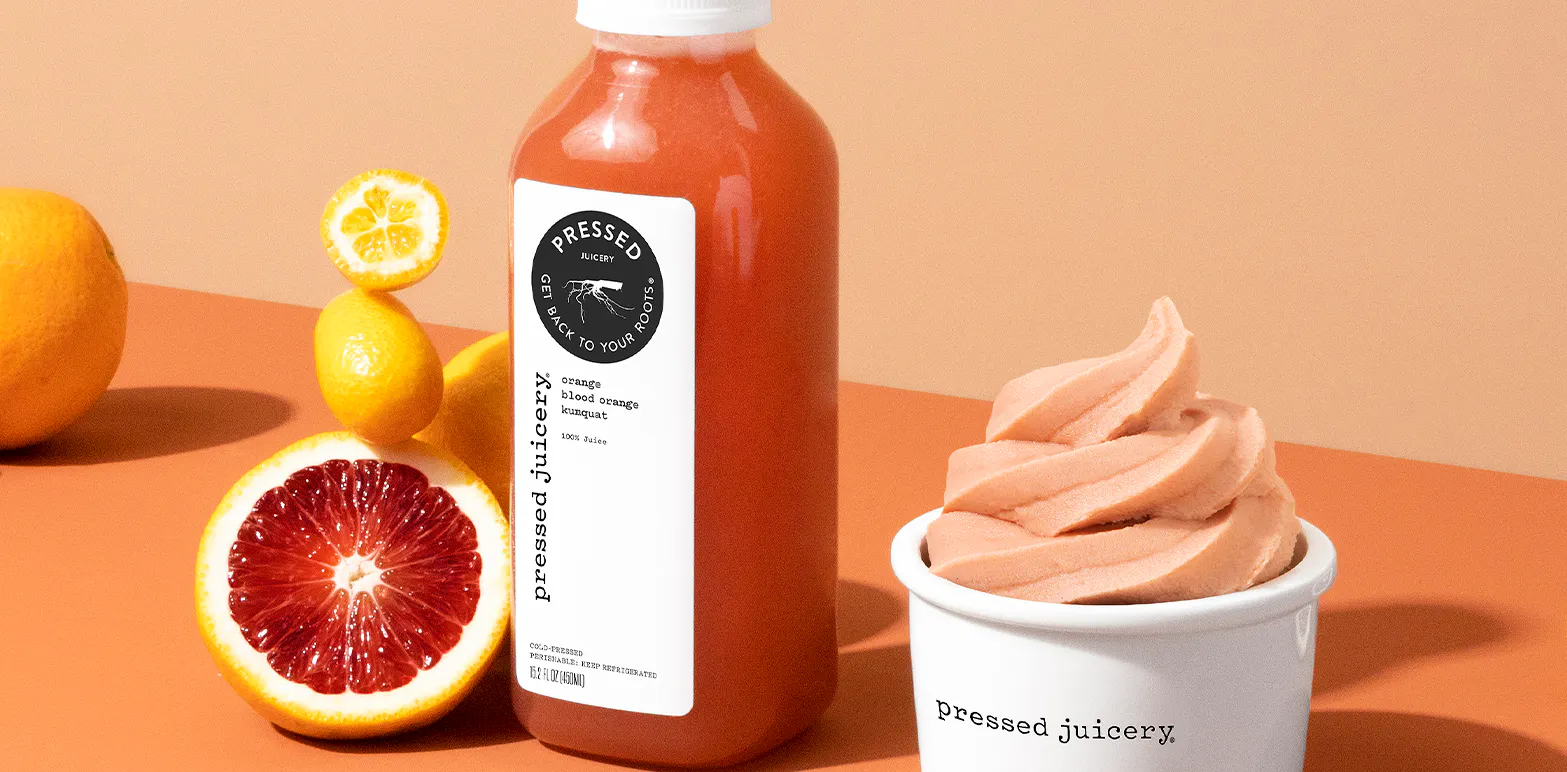 Image of an dark orange pressed juice next to blood oranges on an orange background