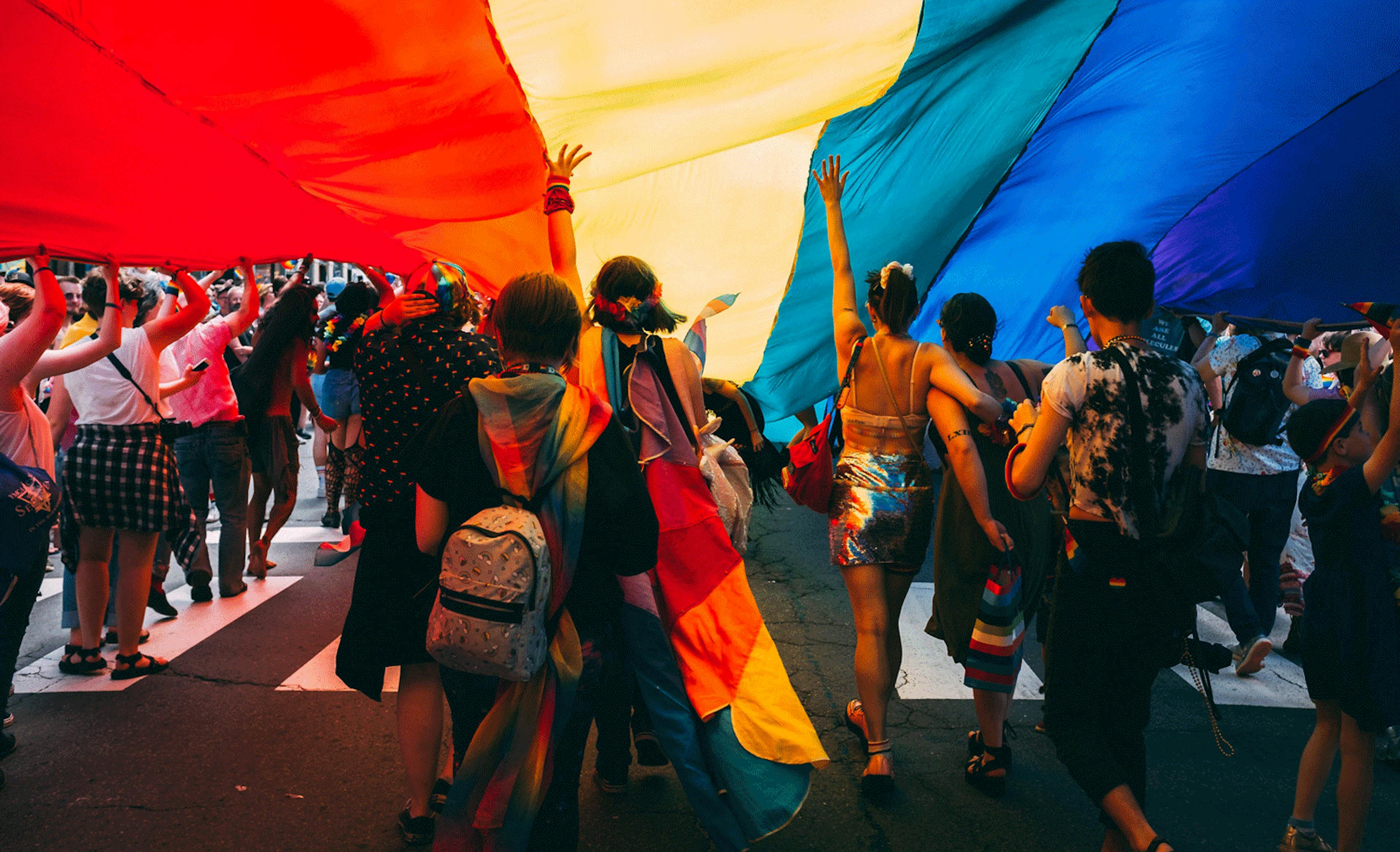 Image of people celebrating pride under a rainbow colored parachute