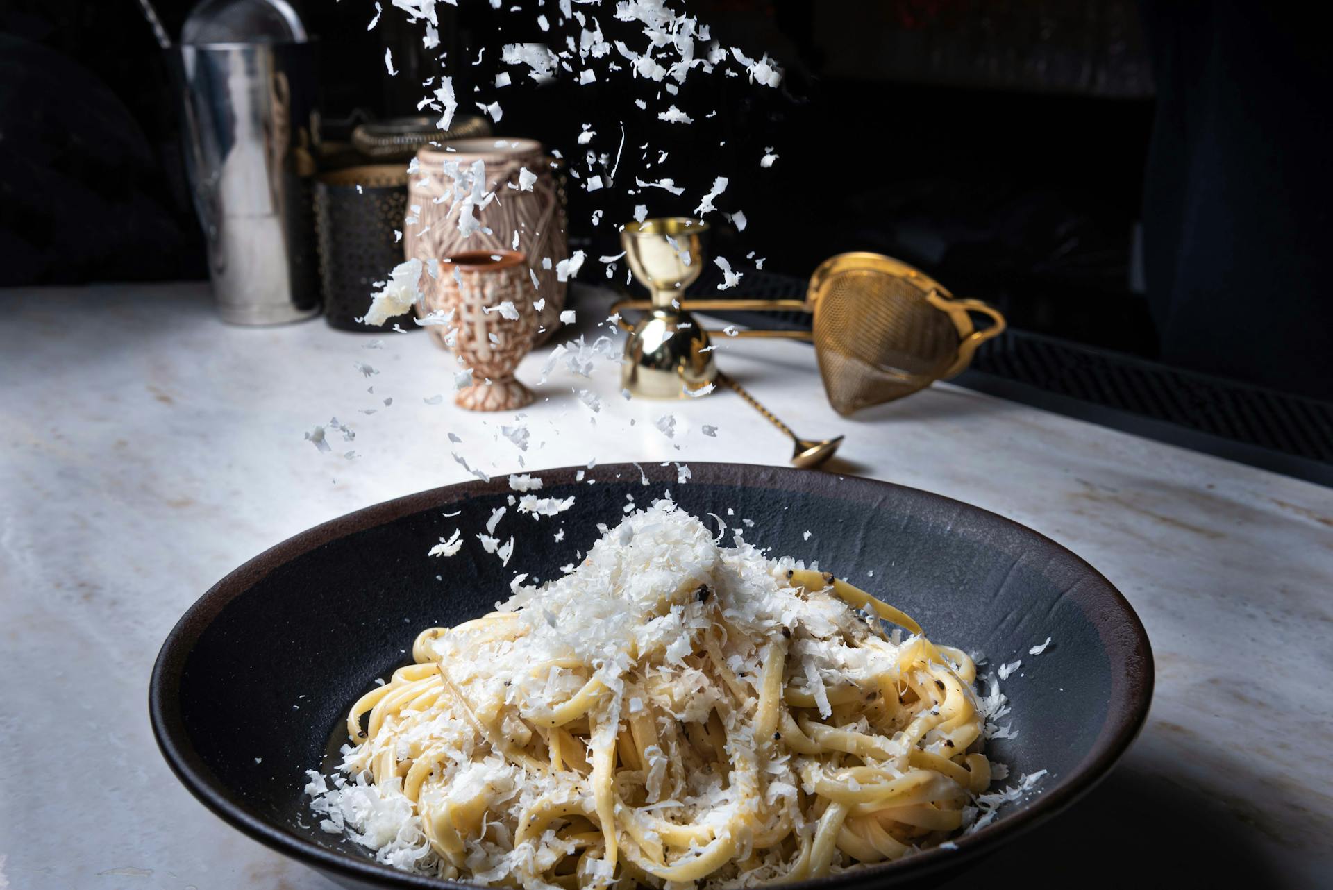 Image of a bowl of pasta with tons of parmesan cheese being grated on top of it