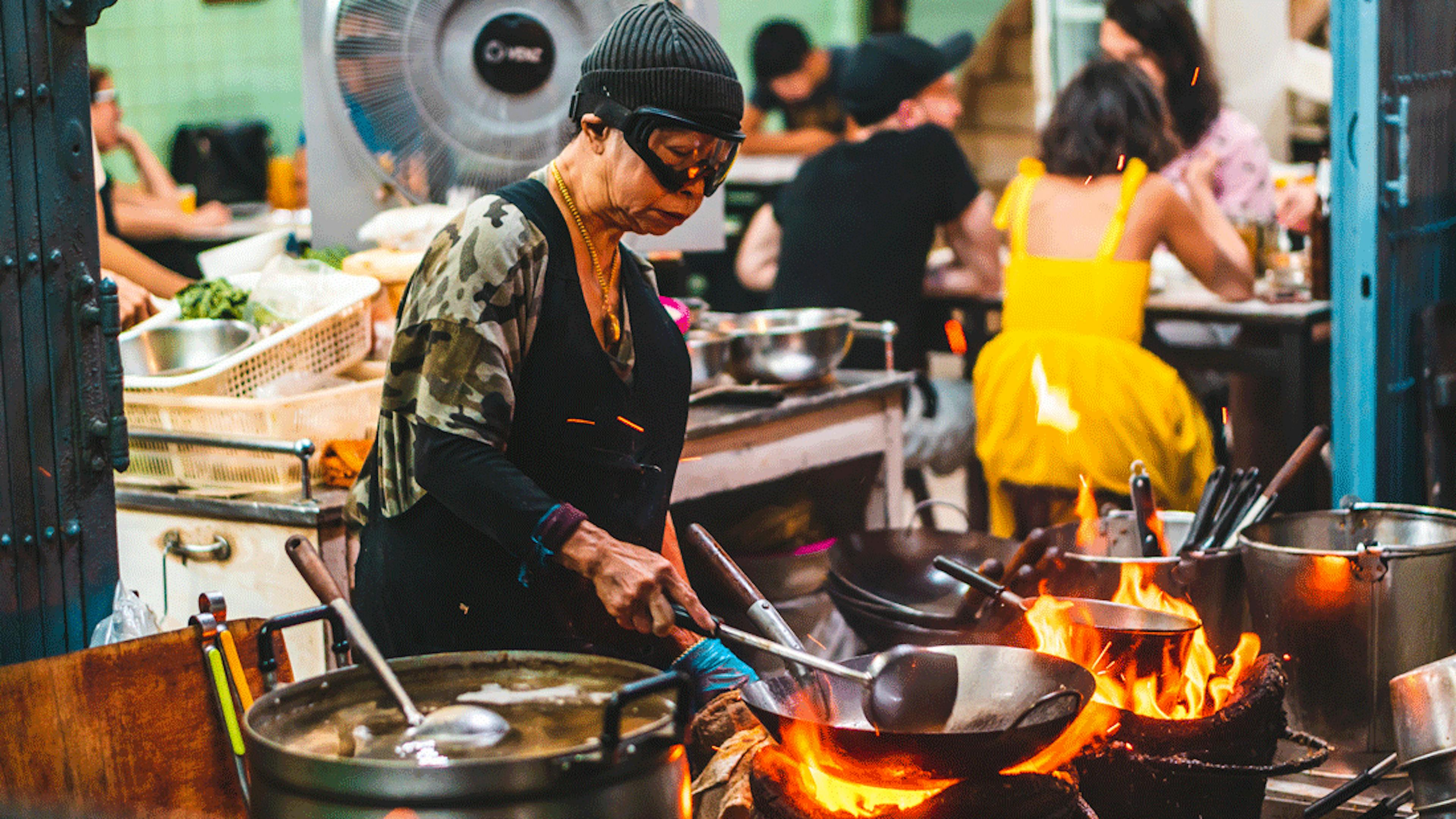 Image of a restaurant owner manning the flame at a hawker style restaurant