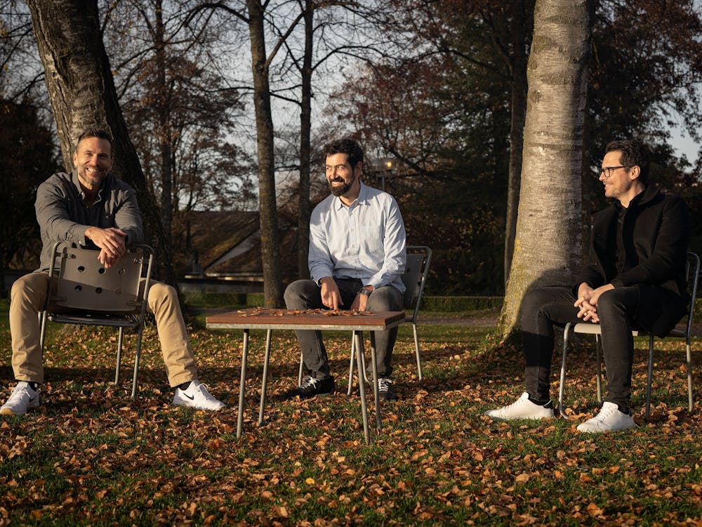 Frank Salathé, Daniel Bossard und Phil Bergdorf sitzen draußen auf Stühlen auf der Wiese