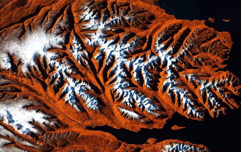 Loftmynd af firði og háum fjöllum í kring. Snjór efsti í fjöllunum.