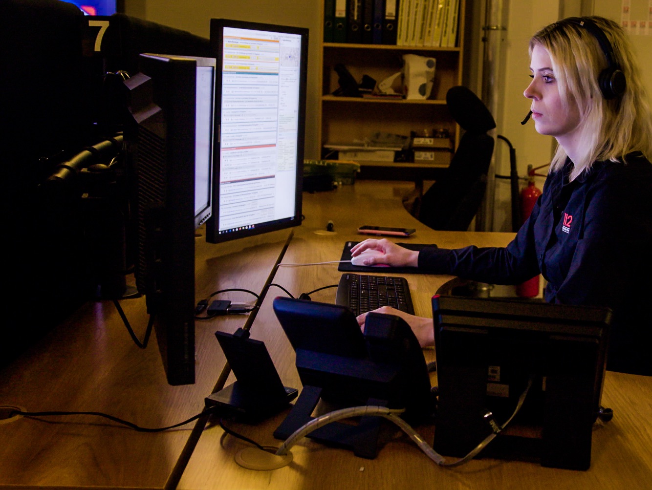 Neyðarvörður við skrifborðið sitt þar sem á eru margir símar og skjáir