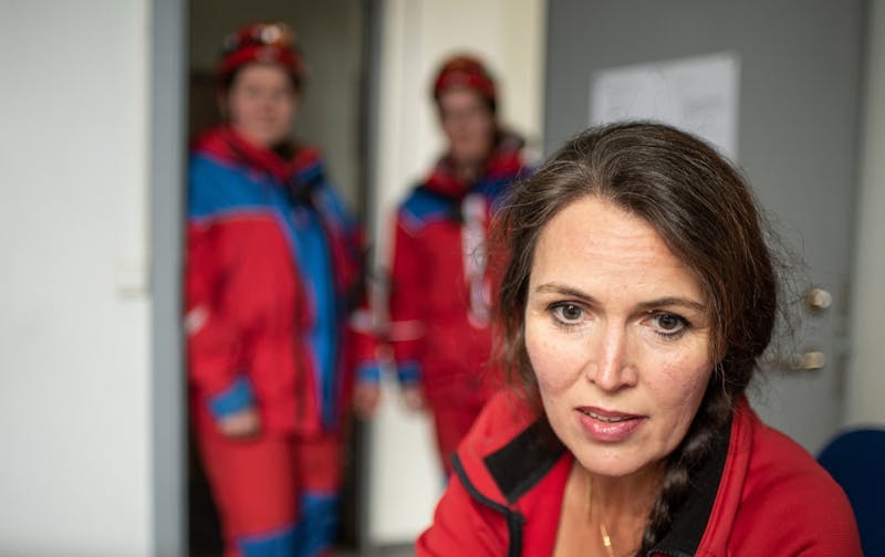 Björgunarsveitarkona í forgrunni er að lesa af tölvuskjá. Í bakgrunni eru tveir björgunarsveitarmenn úr fókus sem virðast bíða eftir upplýsingum.