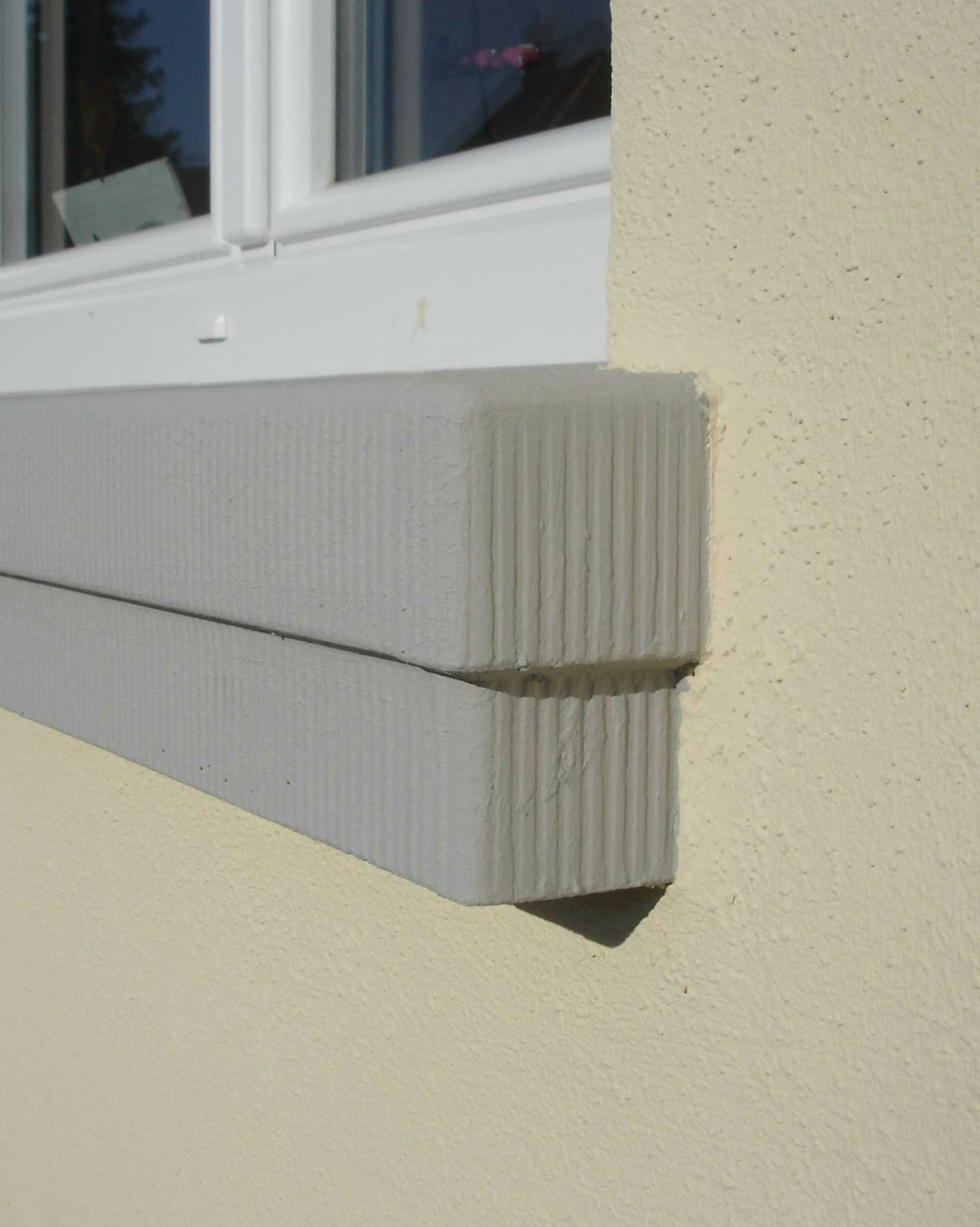 Stark scharrierte Fensterbank SLB 300 an einer gelben Putzfassade