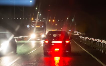 Vue nocturne d'une route avec des halos lumineux autour des phares de voitures et de camions, illustrant les effets d'éblouissement et de diffusion de la lumière.