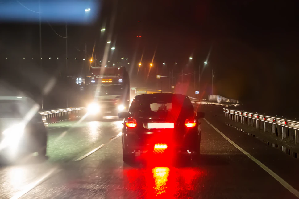 Vue nocturne d'une route avec des halos lumineux autour des phares de voitures et de camions, illustrant les effets d'éblouissement et de diffusion de la lumière.