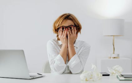 Une femme portant des lunettes avec des verres optiques Nikon cachant son visage avec ses mains, exprimant un sentiment de stress.