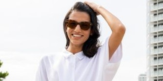Femme portant des verres solaires Nikon avec traitement  SeeCoat Super Sun UV dans un parc avec un immeuble en arrière plan.