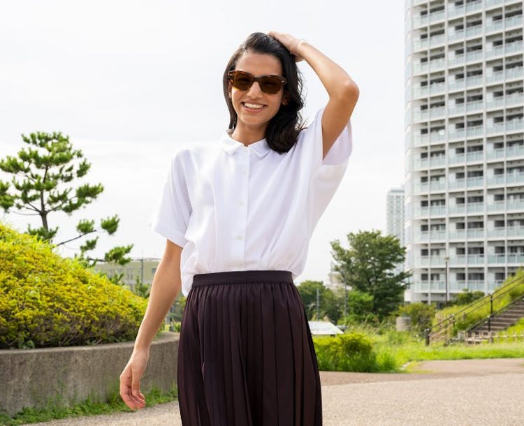 Femme portant des verres solaires Nikon avec traitement SeeCoat Super Sun UV dans un parc avec un immeuble en arrière plan.