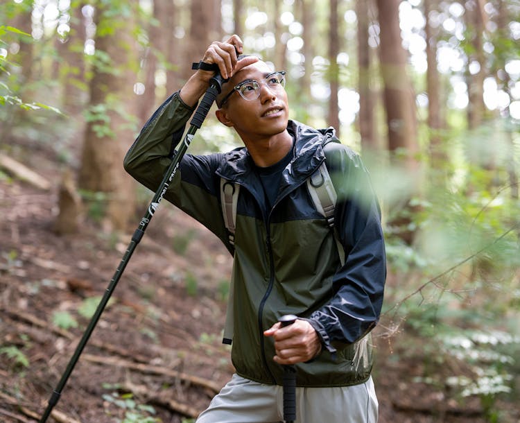 Homme entouré de végétation tenant dans la main un bâton de marche portant une paire de lunettes verres optiques Nikon.