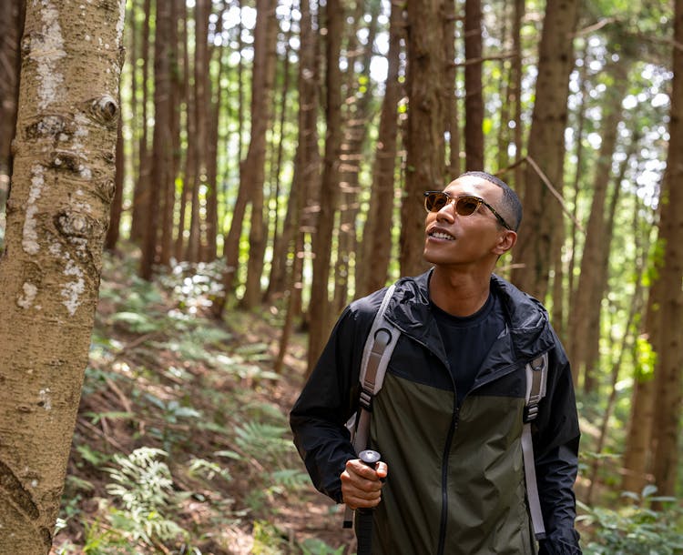 Homme entouré de végétation tenant dans la main un bâton de marche portant une paire de lunettes verres optiques Nikon.