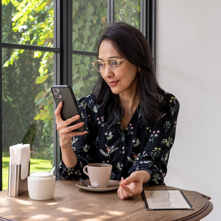 Femme portant une paire de lunettes avec des verres optiques Nikon regardant son téléphone à mi-distance en buvant son café.