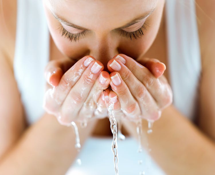 Femme se nettoyant le visage avec de l'eau.