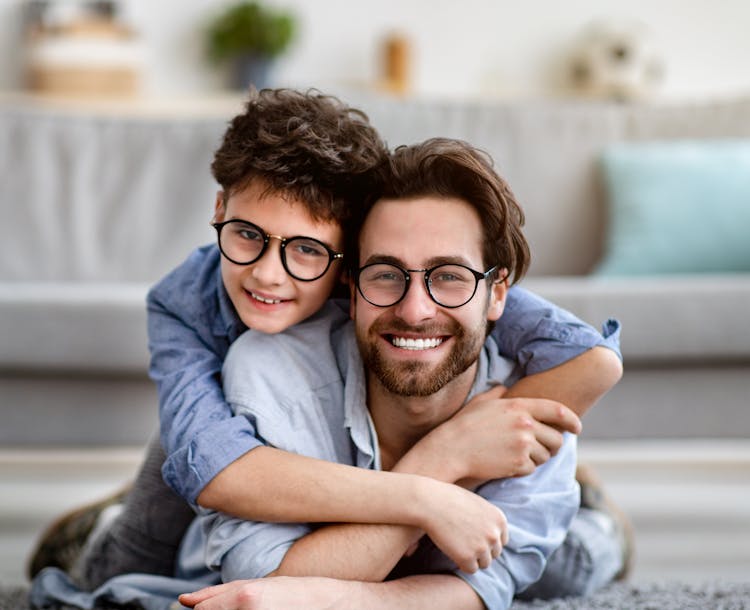 Un père et son fils allongés sur un tapis dans le salon portant une paire de lunettes dotée de verres optiques Nikon.