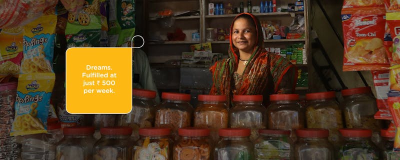 A smiling woman stands behind jars of food in her store.