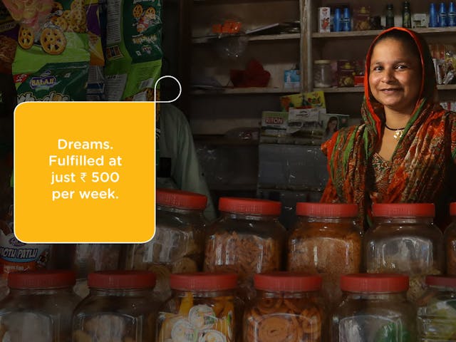 A smiling woman stands behind jars of food in her store.