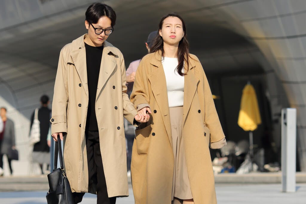 A stylish young couple wearing trench coats as they walk down the street holding hands