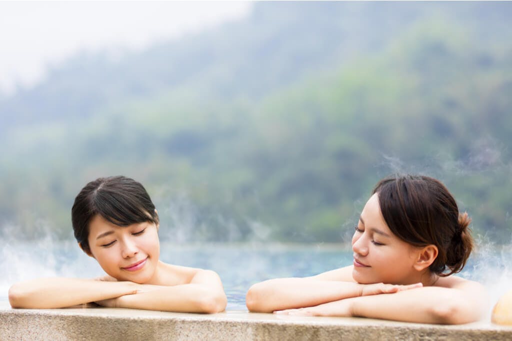 Two Japanese women enjoying a bath at an outdoor onsen. 