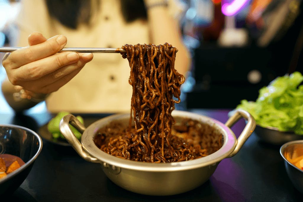 A woman using chopsticks to hold black noodles, a common food for Black Day, in a Korean-Chinese restaurant.
