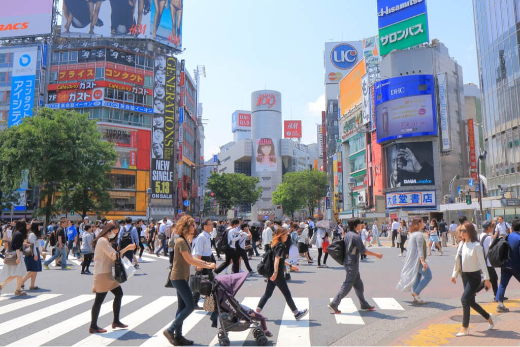 People walking around Shibuya crossing during the day with the 109 building in the center background