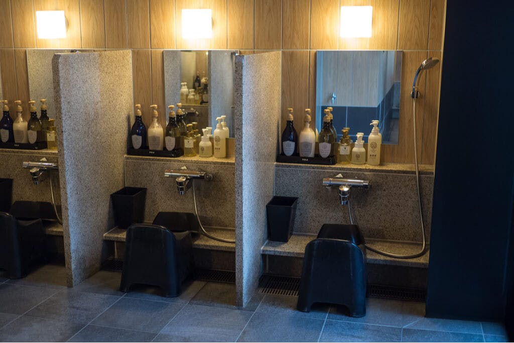 A series of stools in front of showers with mirrors and amenities at a sento