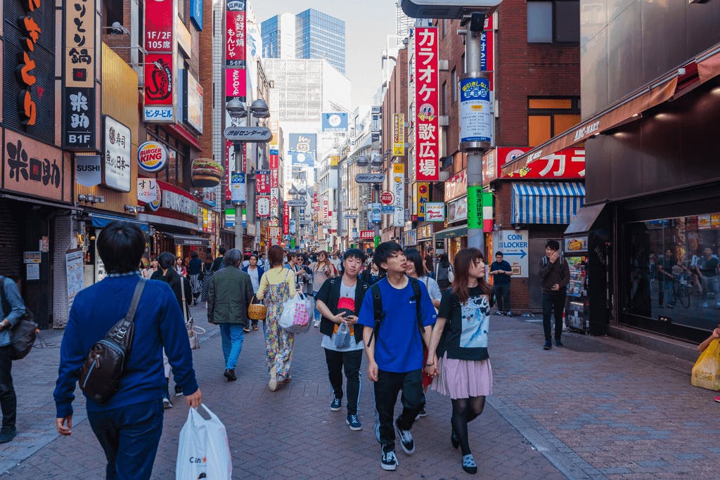 Many people walking down a busy road in Shibuya, a popular date spot in Tokyo, with many restaurants in the background