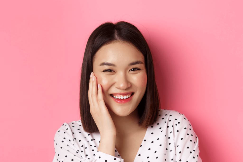 A woman stands in a polka-dot blouse in front of a pink background with makeup using the drunken cheek effect popular in Japanese makeup trends.