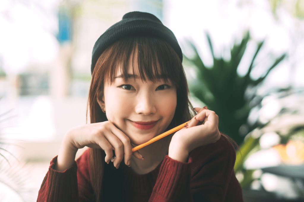 A woman sits in a cafe wearing a cap over her hair and a face of makeup with a puppy dog eyeliner look and red lips