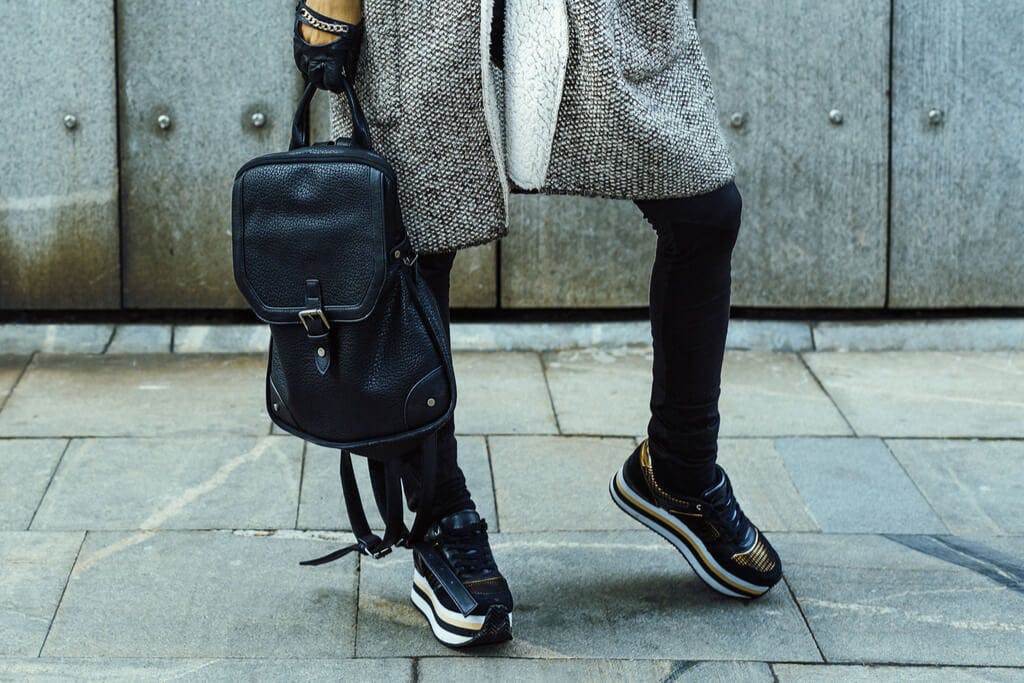 A woman wearing platform sneakers on the sidewalk of a big city while holding a black bag