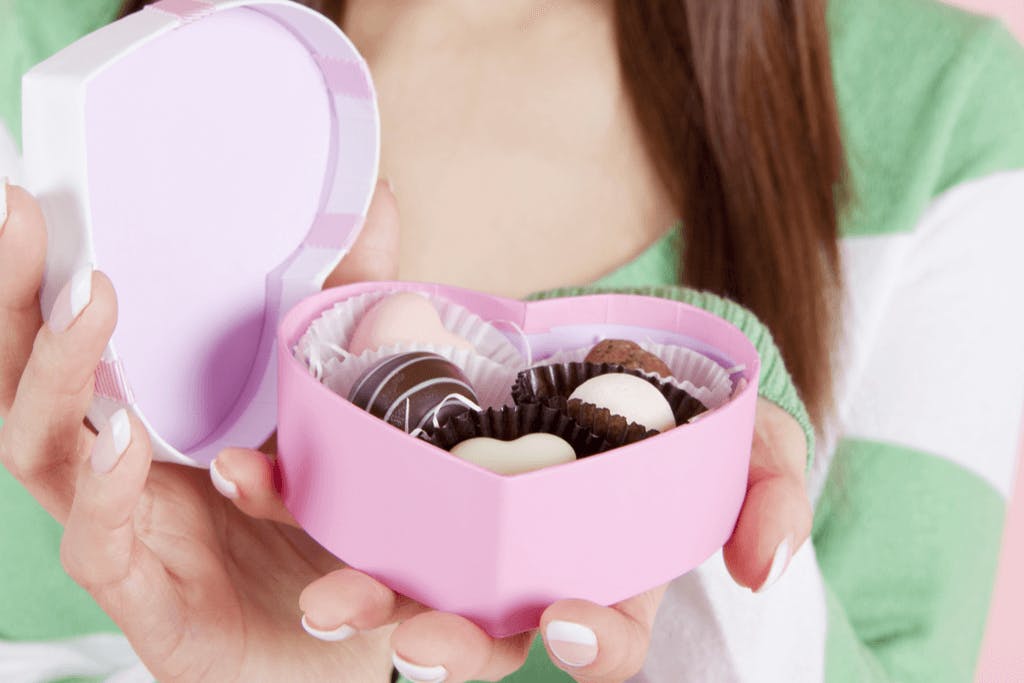 A woman in a white and green sweater presents chocolates in a heart-shaped box for Valentine's Day in Japan.