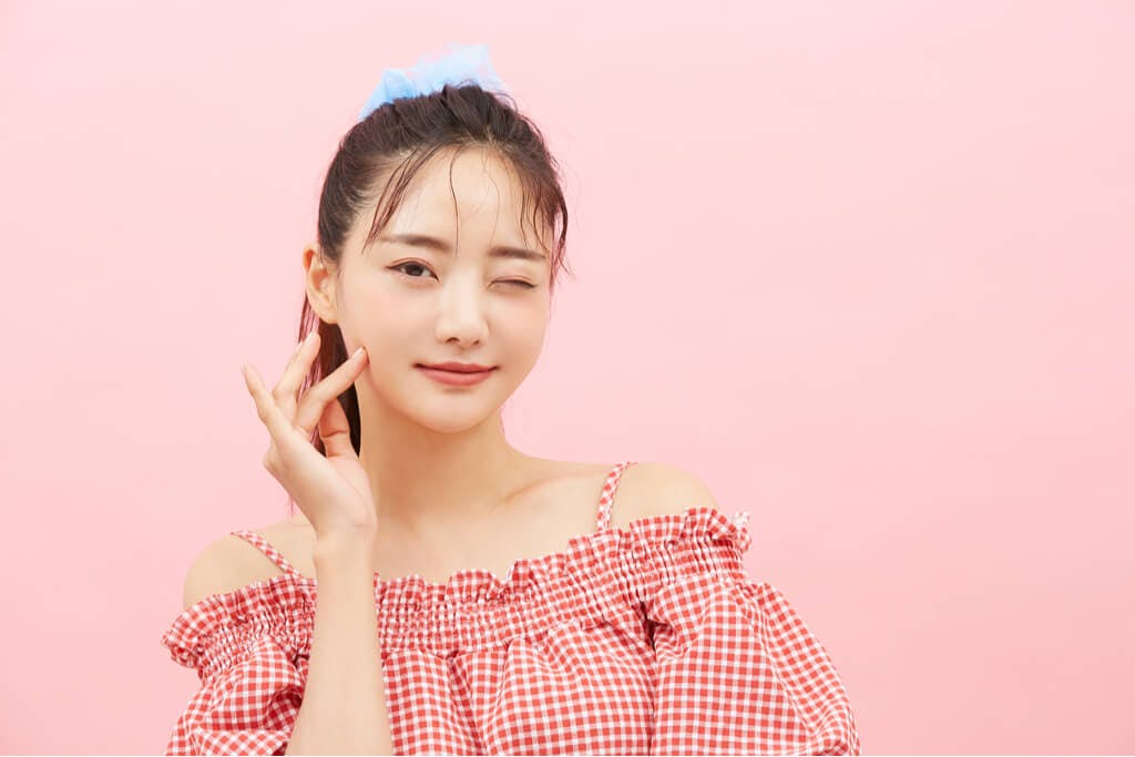 A young woman touches her face and winks after applying her Peach C makeup